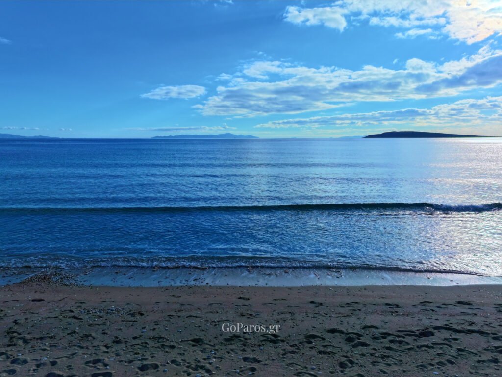 Calm blue waters and sandy shore at Piso Aliki Beach Paros with distant islands on the horizon