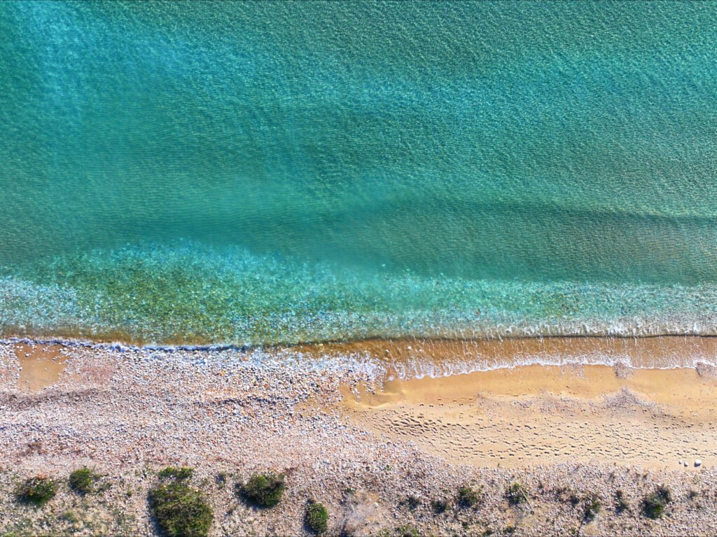 Overhead view of crystal clear turquoise water meeting the sandy beach at Piso Aliki Paros