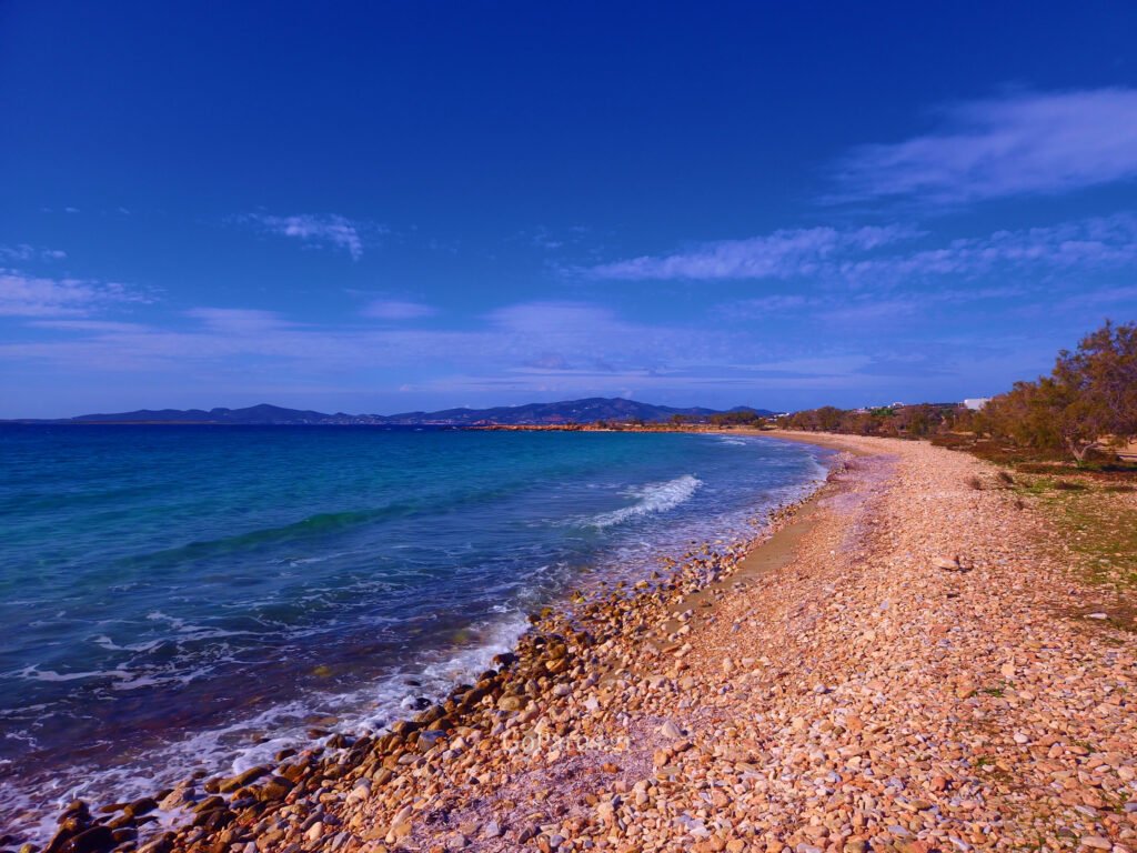 Pebble shoreline at Piso Aliki Beach Paros with gentle waves and scenic mountain backdrop