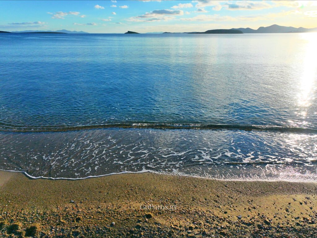 Voutakos Beach, Paros, calm sea at the waterline with sun reflection and distant islands