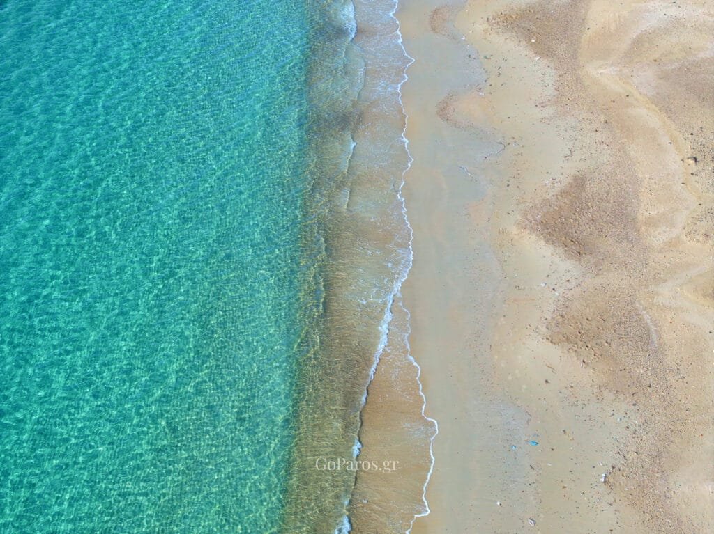Top-down aerial of clear turquoise water meeting the sand at Krios Beach, Paros.