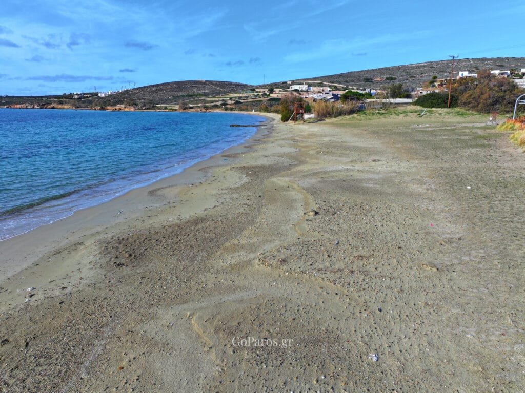 Wide view of Krios Beach bay with calm water, sandy shore and hills in the background, Paros.
