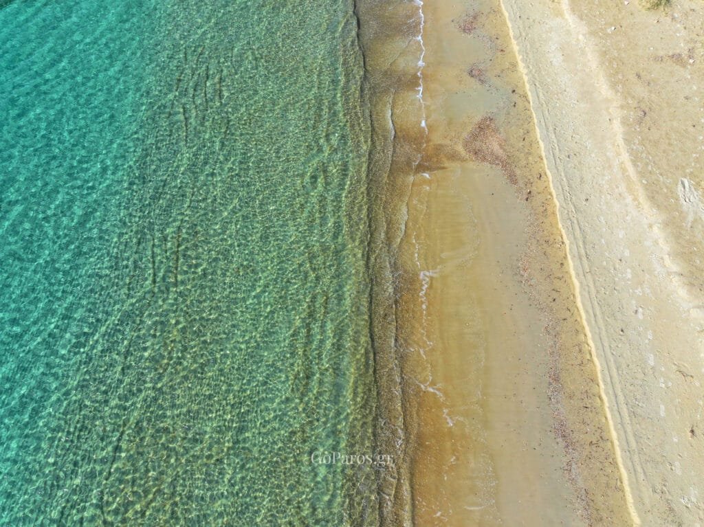 Top-down view of clear water meeting the sand at Marcello Beach, Paros.