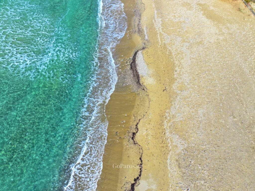 Top-down aerial of the waterline and sand at Parasporos Beach, Paros.