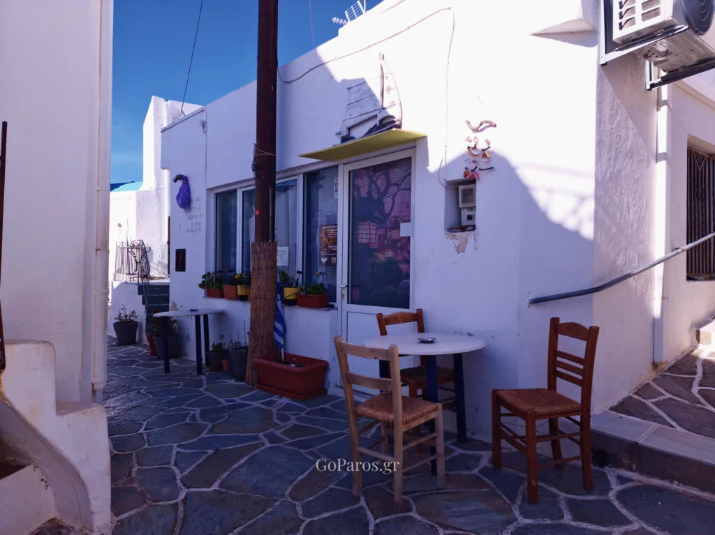 Small village cafe with wooden chairs on a stone-paved lane in Kostos, Paros